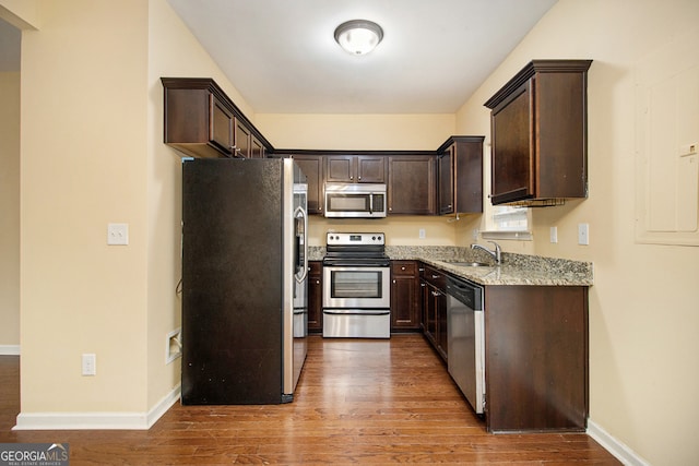 kitchen with appliances with stainless steel finishes, sink, dark brown cabinetry, light hardwood / wood-style flooring, and light stone countertops