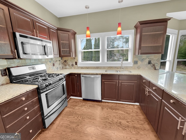 kitchen featuring stainless steel appliances, backsplash, sink, light hardwood / wood-style floors, and hanging light fixtures