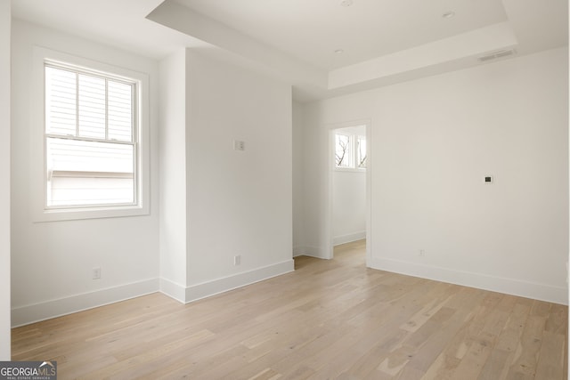 spare room featuring a tray ceiling and light hardwood / wood-style flooring