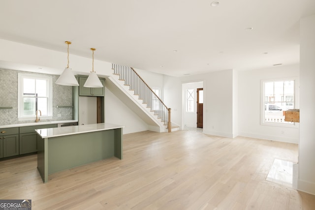 kitchen featuring decorative light fixtures, sink, decorative backsplash, green cabinetry, and light hardwood / wood-style flooring