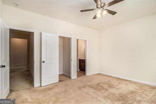 unfurnished bedroom with light colored carpet, connected bathroom, a walk in closet, and ceiling fan