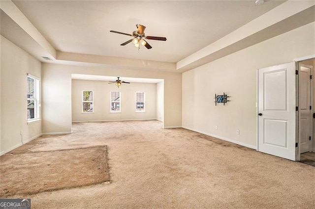 unfurnished living room with ceiling fan, a raised ceiling, and light carpet