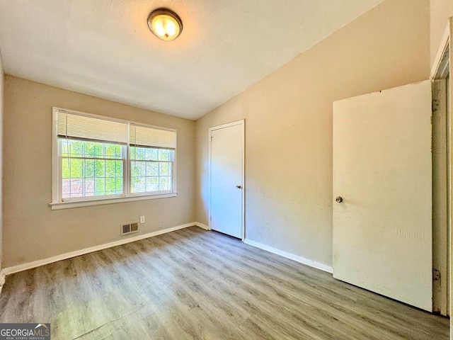 unfurnished bedroom featuring wood-type flooring, vaulted ceiling, and a closet