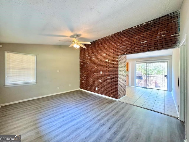 interior space with brick wall, a textured ceiling, ceiling fan, and light wood-type flooring