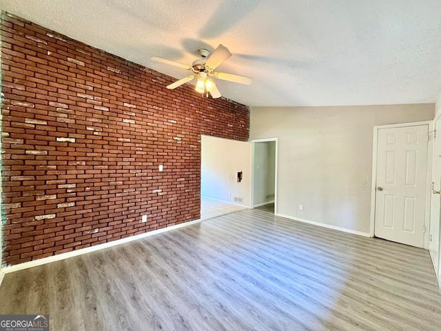 empty room with ceiling fan, brick wall, a textured ceiling, and light wood-type flooring