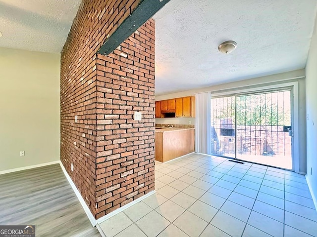 interior space featuring light tile patterned flooring, brick wall, and a textured ceiling