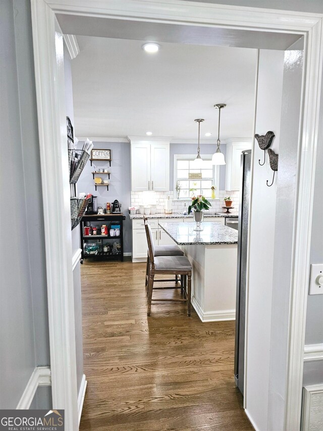 kitchen featuring light stone counters, white cabinets, pendant lighting, dark wood-type flooring, and a breakfast bar