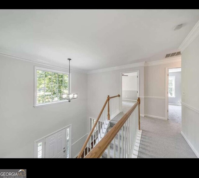 hallway with light colored carpet, crown molding, and a chandelier