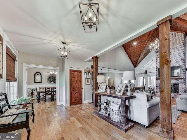 living room featuring a brick fireplace, a notable chandelier, decorative columns, and light hardwood / wood-style flooring