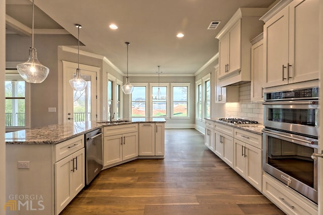 kitchen with light stone countertops, hanging light fixtures, stainless steel appliances, and dark wood-type flooring