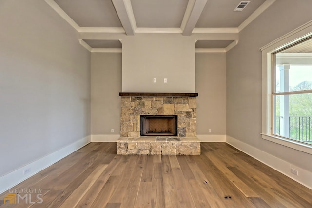 unfurnished living room with dark wood-type flooring, ornamental molding, beam ceiling, and a stone fireplace