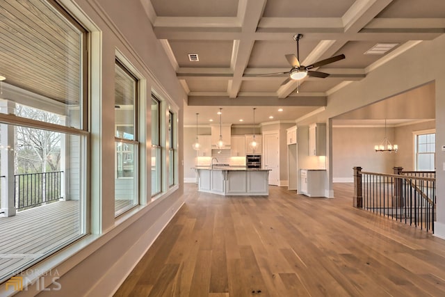 interior space with coffered ceiling, a wealth of natural light, beamed ceiling, light wood-type flooring, and ceiling fan with notable chandelier