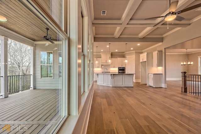 interior space with coffered ceiling, beam ceiling, light wood-type flooring, and ceiling fan with notable chandelier