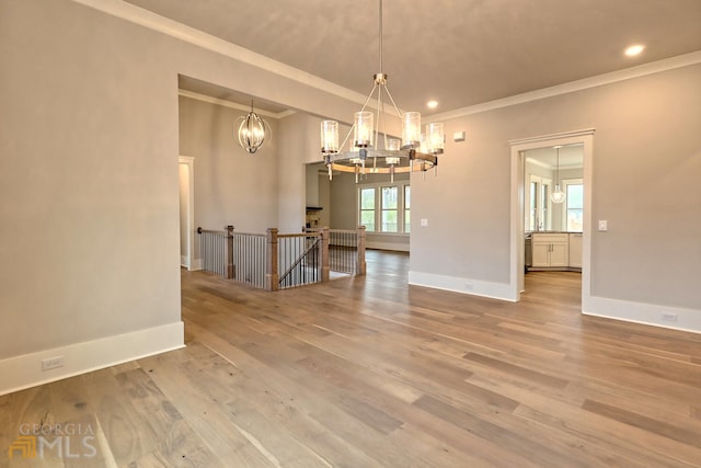 empty room with ornamental molding, a chandelier, and light hardwood / wood-style floors