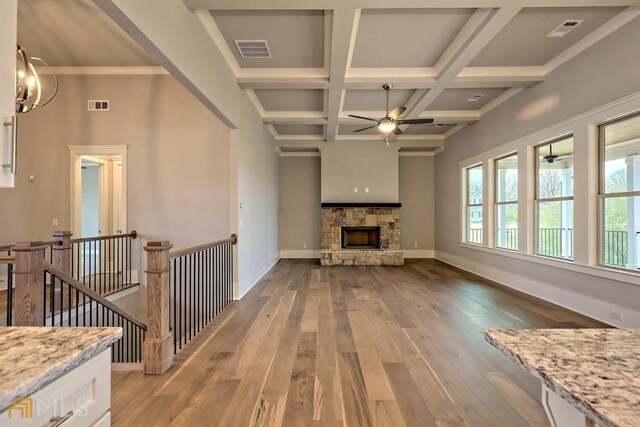 unfurnished living room with a stone fireplace, coffered ceiling, dark hardwood / wood-style floors, and ceiling fan with notable chandelier