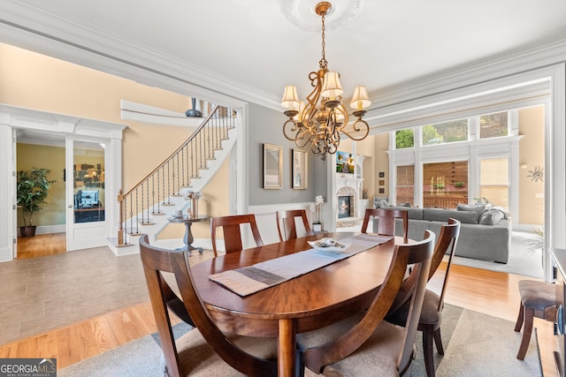 dining room with an inviting chandelier, a stone fireplace, crown molding, and light hardwood / wood-style flooring