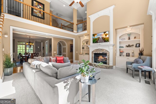 carpeted living room featuring a high ceiling, a stone fireplace, ceiling fan, and built in shelves