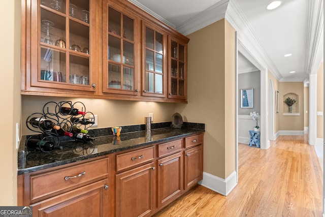 bar with dark stone countertops, light wood-type flooring, and crown molding