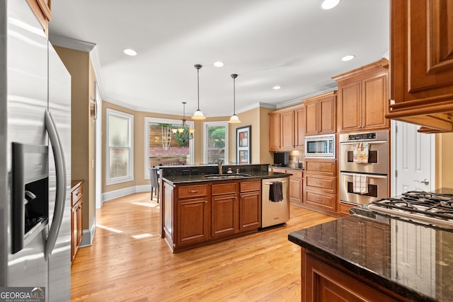 kitchen with light wood-type flooring, stainless steel appliances, crown molding, decorative light fixtures, and a center island with sink