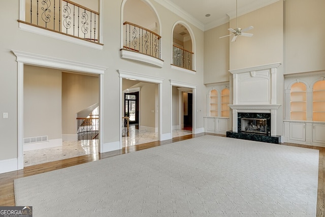 unfurnished living room with ceiling fan, light hardwood / wood-style floors, a premium fireplace, a towering ceiling, and crown molding