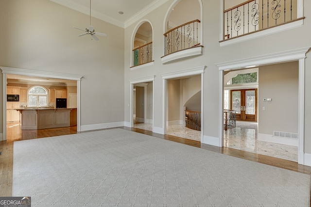 unfurnished living room with french doors, ceiling fan, crown molding, light hardwood / wood-style flooring, and a high ceiling