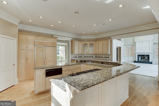 kitchen featuring stone countertops, light hardwood / wood-style floors, a premium fireplace, a kitchen island, and crown molding