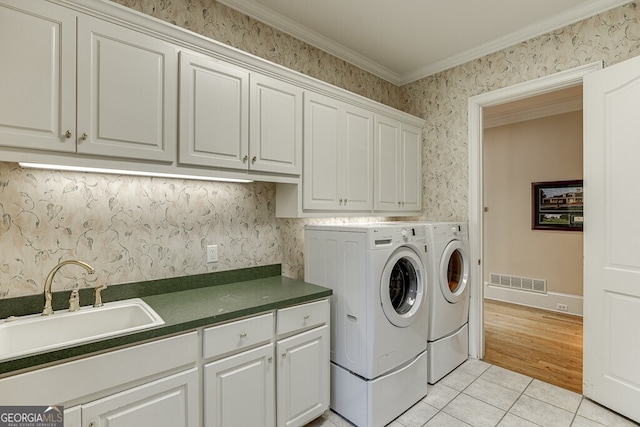 clothes washing area featuring light tile floors, cabinets, crown molding, washer and clothes dryer, and sink