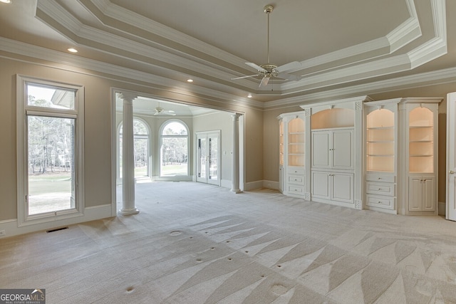 unfurnished bedroom featuring light carpet, ornate columns, multiple windows, and a raised ceiling