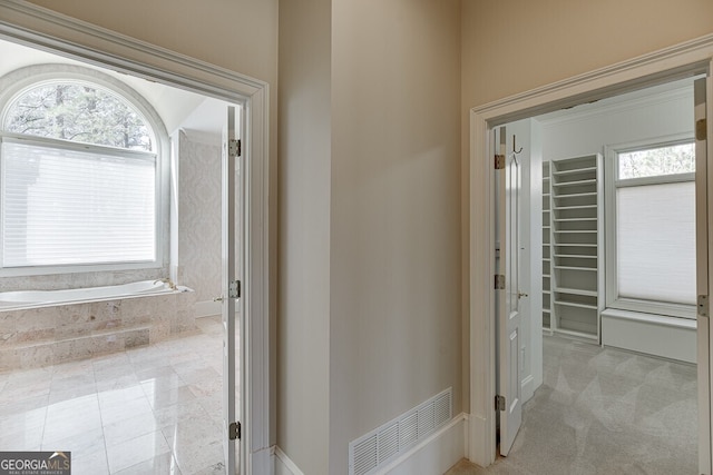 bathroom featuring a relaxing tiled bath, tile floors, and a healthy amount of sunlight