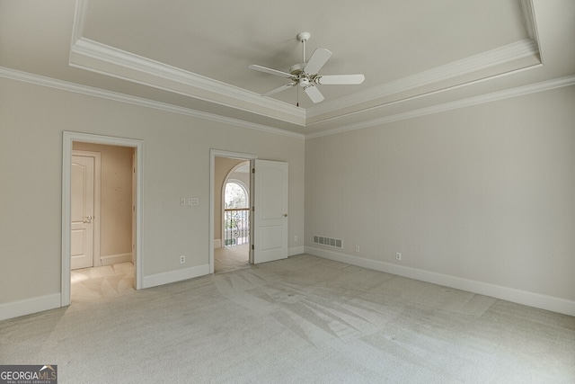 unfurnished bedroom with ceiling fan, ornamental molding, a tray ceiling, and light carpet