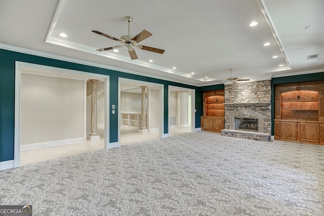 unfurnished living room featuring a stone fireplace, a tray ceiling, ceiling fan, and light colored carpet