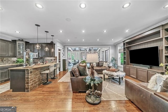 living room with ornamental molding, sink, and light wood-type flooring