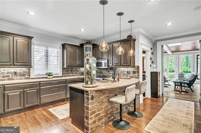 kitchen with wood-type flooring, decorative light fixtures, a breakfast bar area, tasteful backsplash, and an island with sink