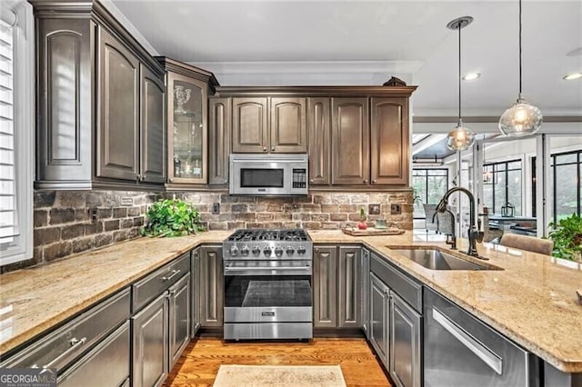 kitchen with decorative light fixtures, light wood-type flooring, stainless steel appliances, sink, and tasteful backsplash