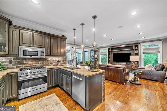 kitchen with light stone countertops, hanging light fixtures, stainless steel appliances, sink, and light wood-type flooring