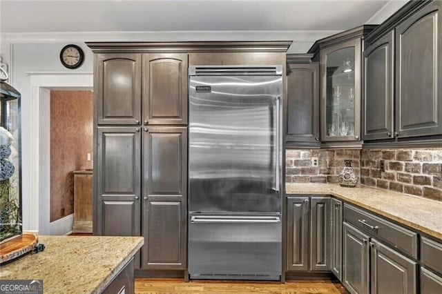 kitchen featuring tasteful backsplash, light wood-type flooring, dark brown cabinets, built in fridge, and light stone countertops