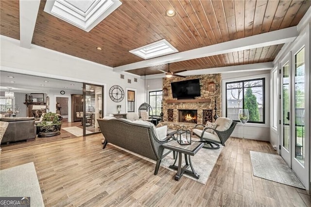 living room with wood ceiling, a skylight, light wood-type flooring, and a stone fireplace