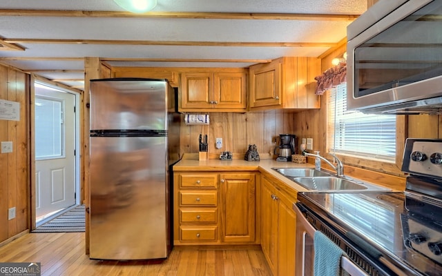 kitchen featuring appliances with stainless steel finishes, sink, light hardwood / wood-style flooring, beam ceiling, and a textured ceiling