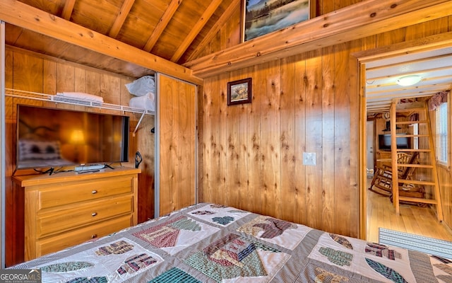 bedroom featuring a closet, hardwood / wood-style floors, wooden ceiling, lofted ceiling with beams, and wooden walls