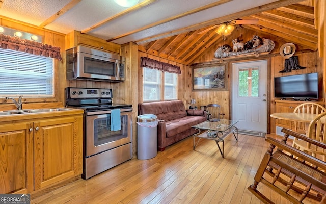 kitchen featuring wooden walls, vaulted ceiling with beams, light wood-type flooring, and stainless steel appliances