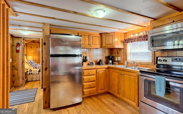 kitchen with wood walls, stainless steel appliances, beamed ceiling, light hardwood / wood-style flooring, and sink