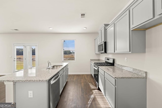 kitchen with light stone countertops, appliances with stainless steel finishes, a healthy amount of sunlight, sink, and a center island with sink