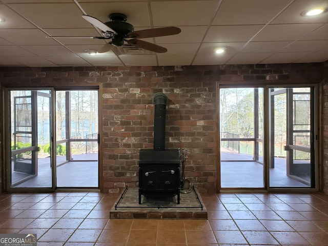 unfurnished living room featuring a paneled ceiling, a healthy amount of sunlight, brick wall, and ceiling fan