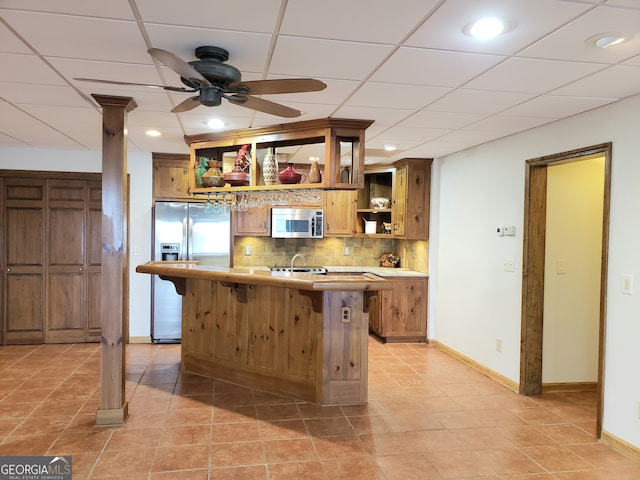 kitchen featuring backsplash, ceiling fan, appliances with stainless steel finishes, light tile floors, and a drop ceiling