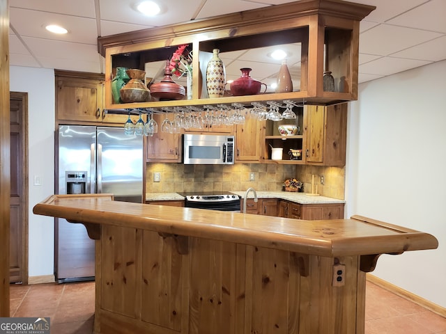 bar with wood counters, stainless steel appliances, light tile floors, a drop ceiling, and backsplash