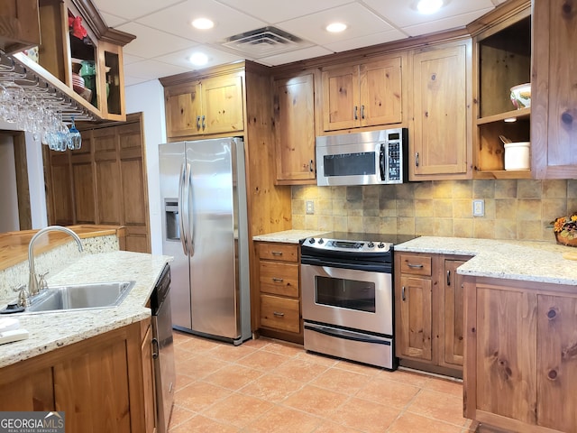 kitchen featuring stainless steel appliances, light tile floors, light stone countertops, backsplash, and sink