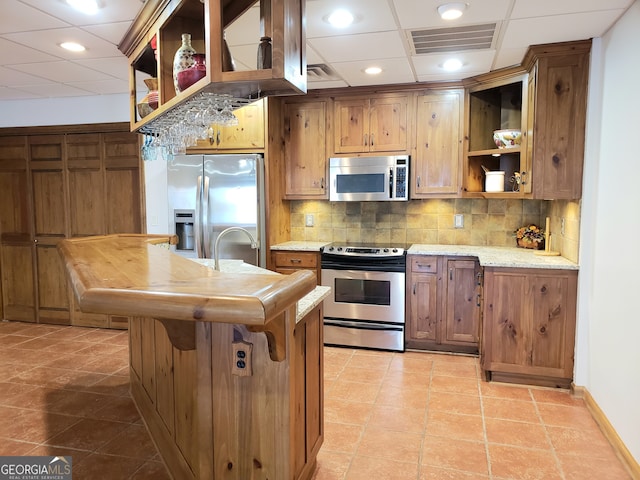 kitchen with tasteful backsplash, stainless steel appliances, a drop ceiling, and light tile floors