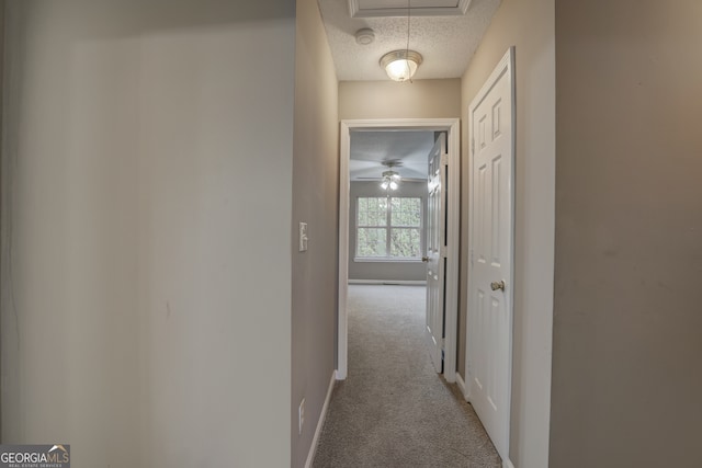 hallway with light carpet and a textured ceiling