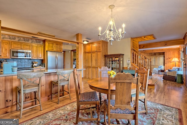 dining space with a chandelier, light hardwood / wood-style flooring, and wooden walls