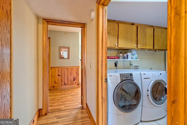 clothes washing area featuring light wood-type flooring, washing machine and clothes dryer, and cabinets